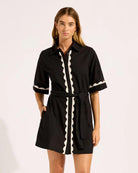 Woman wearing a black cotton t-shirt button down dress with white scalloped trim 
