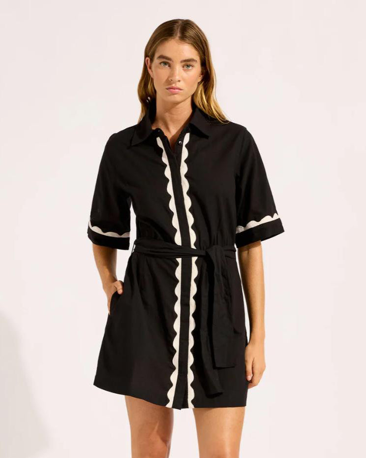 Woman wearing a black cotton t-shirt button down dress with white scalloped trim 