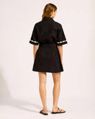 Woman wearing a black cotton t-shirt button down dress with white scalloped trim 