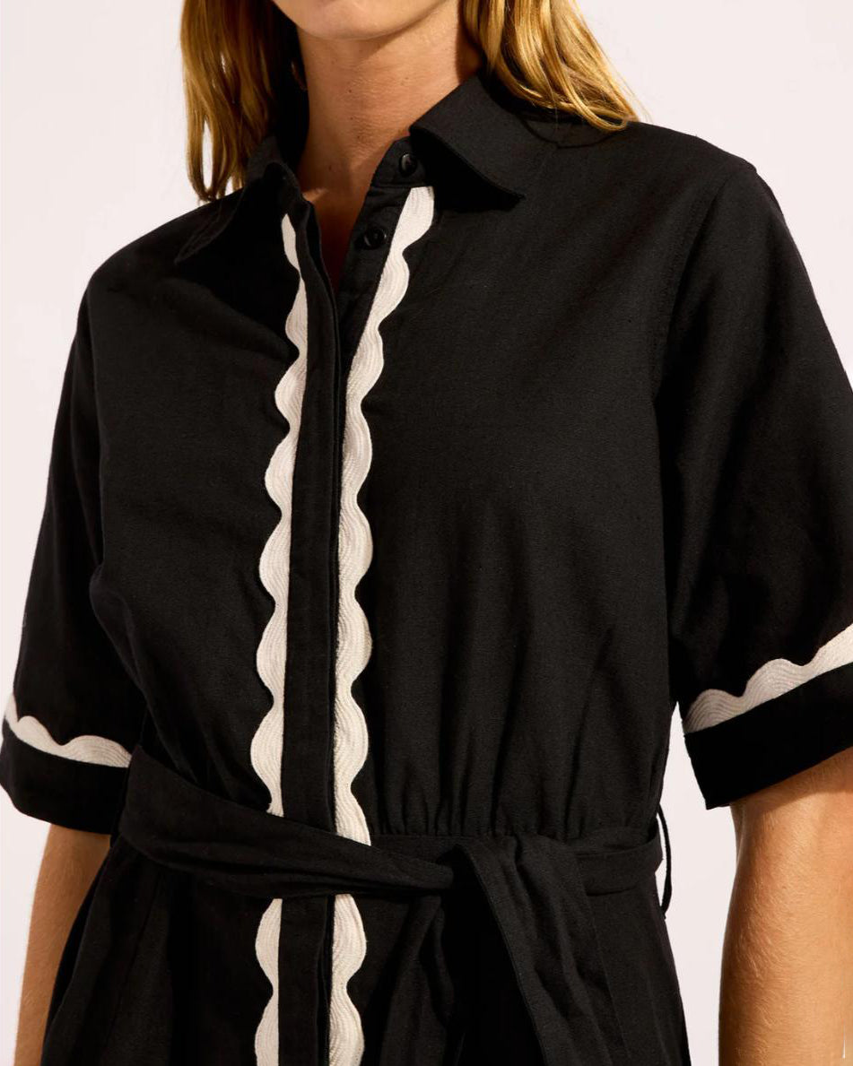 Woman wearing a black cotton t-shirt button down dress with white scalloped trim 