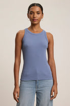 A woman wearing a blue ribbed tank top and grey trousers