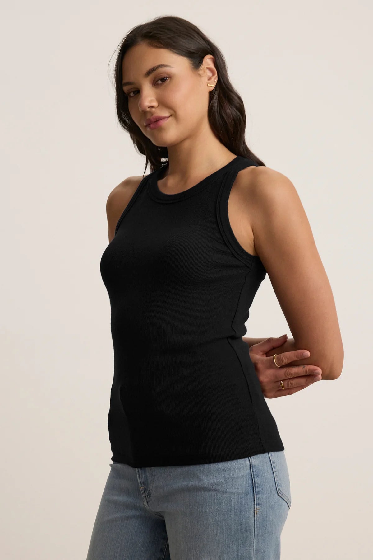 A woman wearing a black ribbed tank top and grey trousers