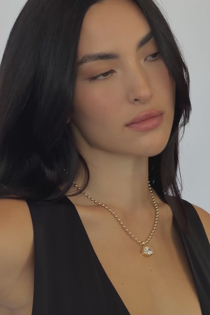A video of a woman wearing  gold chain necklace with a big oval crystal pendant by brand Lili Claspe