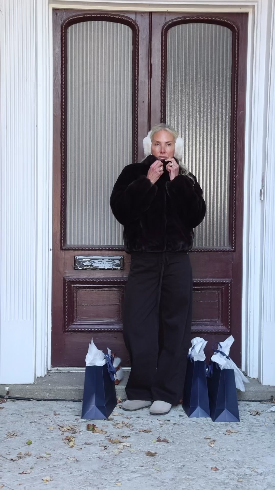 A woman wearing a faux fur short coat and fuzzy earmuffs has shopping bags