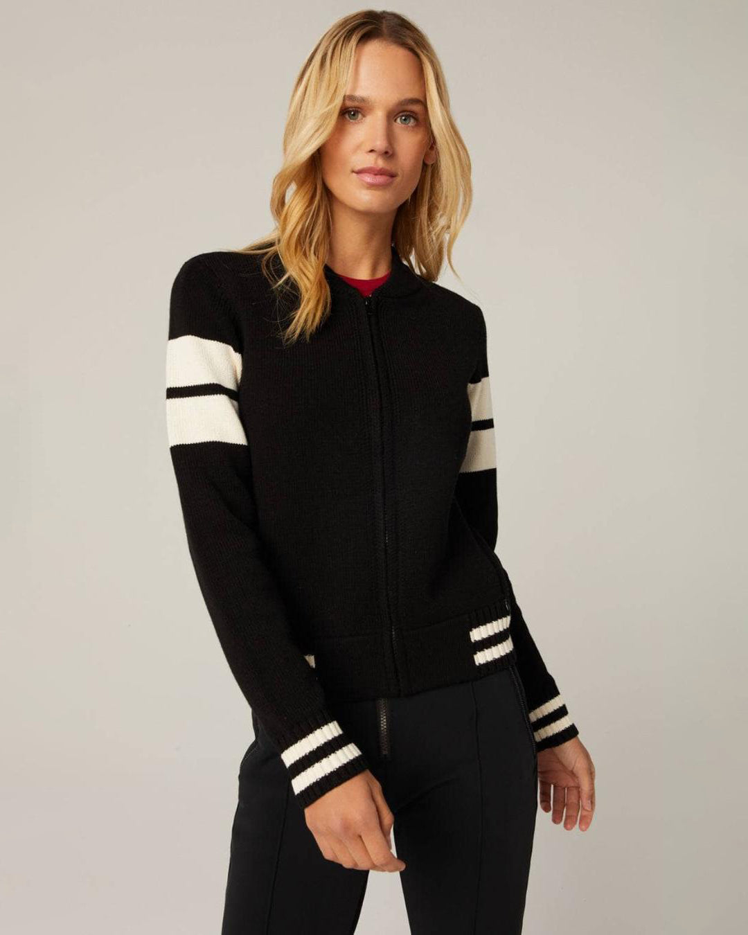 Woman wearing a black zip up cardigan jacket with white stripes and a skier on the back