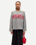 Person wearing a gray sweater with red text that says the brand 'SAMSOE'