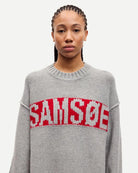 Person wearing a gray sweater with red text that says the brand 'SAMSOE'