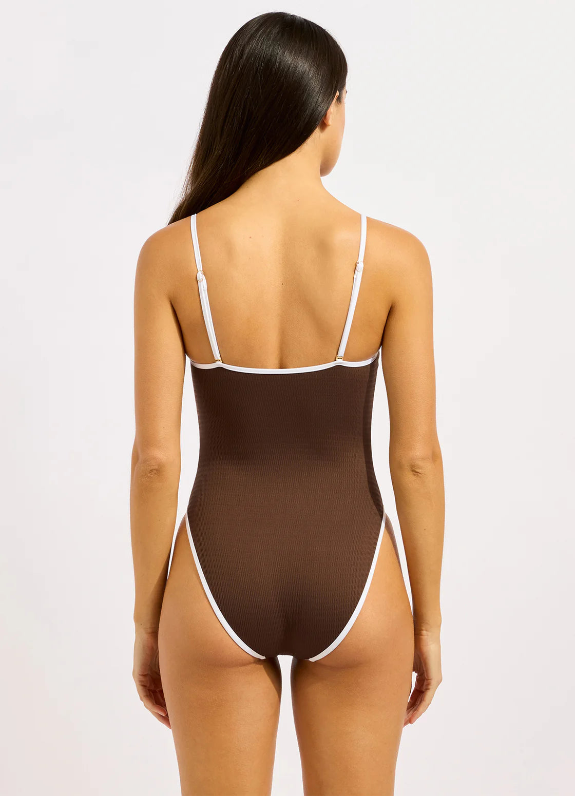 A woman wearing a brown ribbed one-piece swimsuit with thin white contrast trim and spaghetti straps by Seafolly