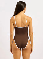 A woman wearing a brown ribbed one-piece swimsuit with thin white contrast trim and spaghetti straps by Seafolly