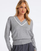 Woman wearing a v neck knit sweater in grey with white trim