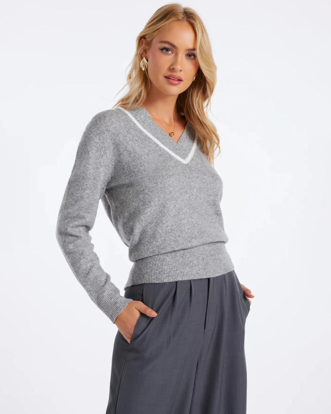 Woman wearing a v neck knit sweater in grey with white trim