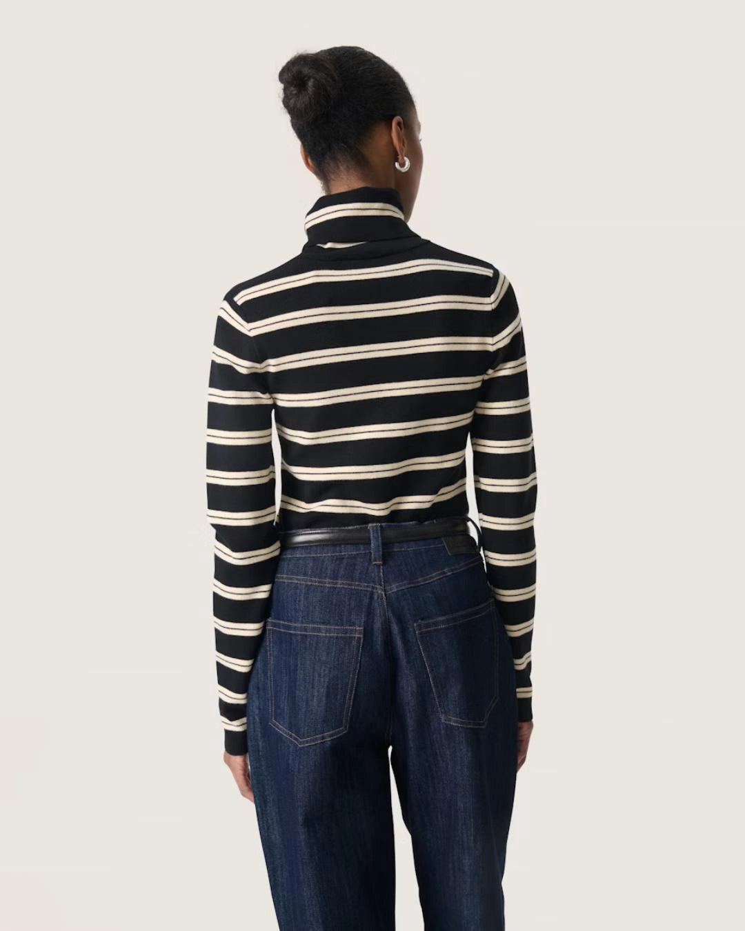 a woman wears a striped black and cream turtleneck polo pullover sweater