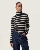 a woman wears a striped black and cream turtleneck polo pullover sweater