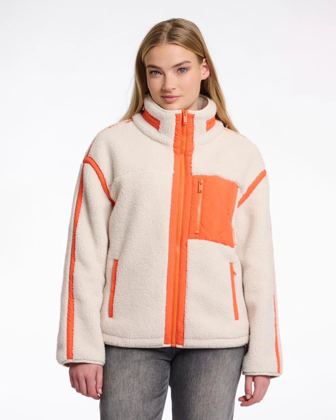 A woman wearing a teddy zip jacket in birch and orange pocket and lining