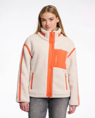 A woman wearing a teddy zip jacket in birch and orange pocket and lining