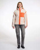 A woman wearing a teddy zip jacket in birch and orange pocket and lining