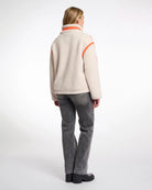 A woman wearing a teddy zip jacket in birch and orange pocket and lining