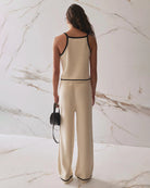 Woman wearing a beige tank top and pants with black trim and matching pants