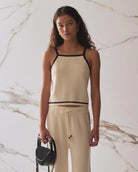Woman wearing a beige tank top and pants with black trim 