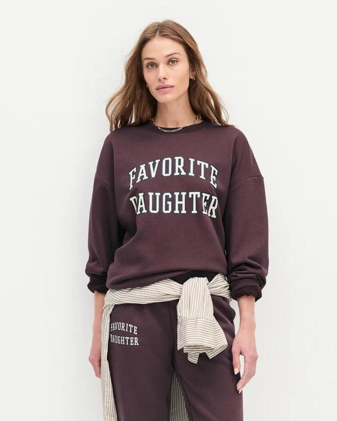 Woman wearing a maroon 'FAVORITE DAUGHTER' sweatshirt and matching sweatpants