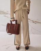 A woman wearing wide leg knit pant in beige with a black stripe on the sides
