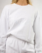woman wearing a white crew neck sweatshirt with embroidery on the chest