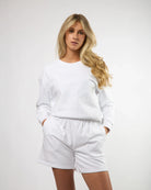 woman wearing a white crew neck sweatshirt and matching shorts with embroidery on the chest